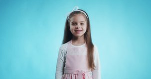Cute Caucasian kid girl wearing pink dress  against blue wall with a happy and cool smile on face. Lucky child