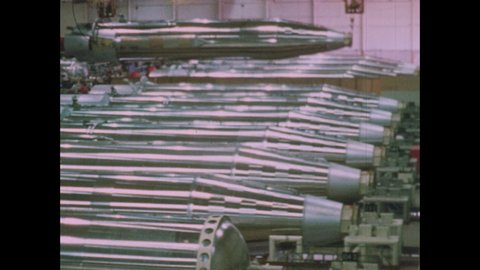 1960s: ICBM Missile body and base is lifted and moved above a long row of other missiles and lowered into place.