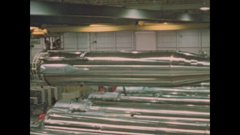 1960s: ICBM Missile body is lifted and moved above a long row of other missiles.