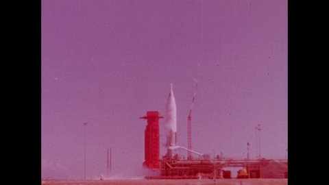 1960s: ICBM Missile is vertical on launch pad as smoke and emissions surround it.