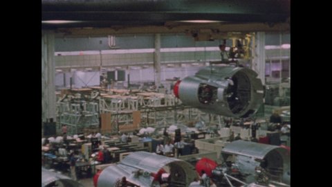 1960s: ICBM Missile base is lifted and moved above a long row of other missiles and lowered into place at end of missile.