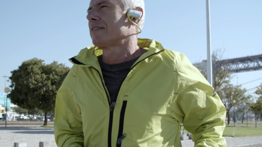 Senior jogger wearing smartwatch, running outside. Elderly man in sporty clothes keeping fit, jogging down street. Cropped shot. Elderly age and lifestyle concept