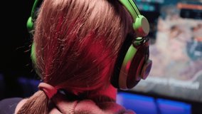 Back view of a young woman playing a video game in the dark with headphones. Esports. 4k video. Blue and red light.
