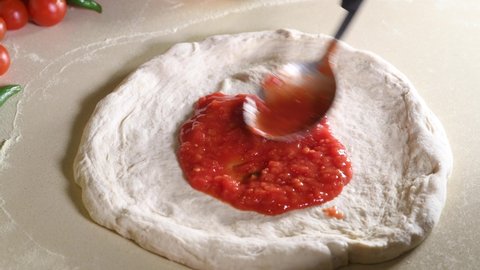 Making italian pizza in Napoli: CloseUp of Chef is spreading Tomato Sauce on Pizza Dough with a Metal Ladle in Traditional Italian Pizza Restaurant. Cooking traditional Sauce for Italian Pizza. 