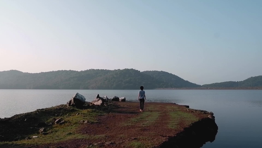 Person Walking At The Edge Of The Coast Overlooking Scenic Mountain And Lake View Of Chapoli Dam Reservoir - wide shot