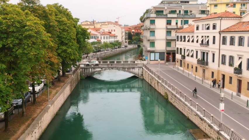 AERIAL: Beautiful canal in Treviso, Italy with a bicycle crossing a stone bridge.