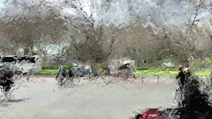 Water runs along a glass wall, people walk behind the glass wall along which the water runs