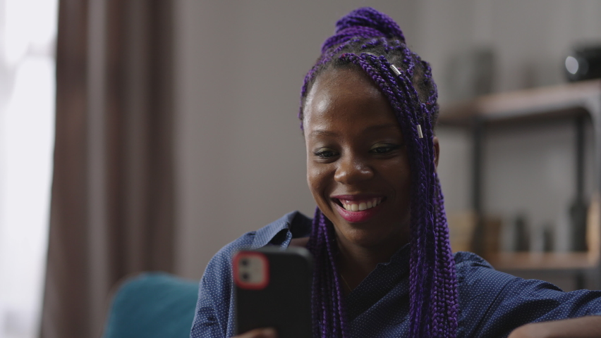 cheerful black woman is chatting by video call in smartphone and smiling broadly, laughing looking at display, resting at home, portrait of nigerian or creole lady in apartment Royalty-Free Stock Footage #1069817482