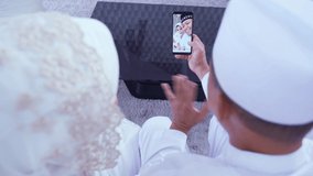 Happy Muslim young couple doing video call with their grandparents during Eid Mubarak while sitting in the living room at home. Shot in 4k resolution