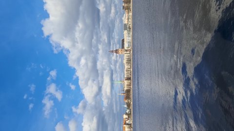 Riga city panorama on the Daugava river in spring on a sunny day. Beautiful white clouds are reflected in the waves. Video rotated 90 degrees.