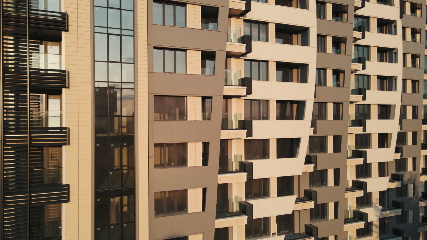 Building Exterior Aerial view of new house city multi-story apartment building - facade, windows and balconies in sunshine at sunset background. Skyscraper Building in Process of Construction. Rent
