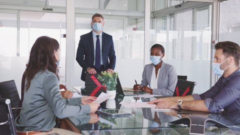Group of multiethnic business people in meeting wearing face mask in conference room during covid19 pandemic. Business workers discussing strategy while wearing masks keeping social distancing.