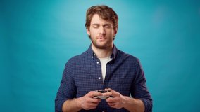 Young bearded man plays pc game with joystick console against blue background