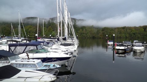 Sailing boats in packed marina on Lake Windermere, Cumbria, English Lake District. Blue sky, clouds, reflections and forest backdrop. Bowness-on-Windermere, Cumbria, UK October 1 2020