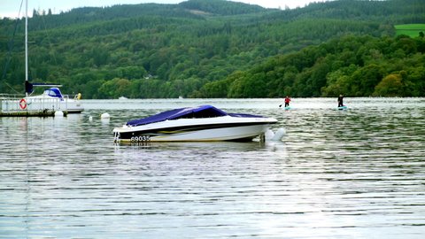 Speedboat moored on scenic lake with forest backdrop and reflections. 4k panorama with blue white boat on Lake Windermere. Ambleside, Cumbria UK October 01 2020
