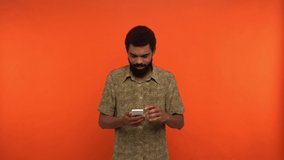 excited african american man messaging on smartphone isolated on orange
