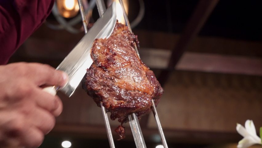 Gaucho slices juicy beef from skewer at Brazilian steakhouse, slow motion 4K Royalty-Free Stock Footage #1069835626