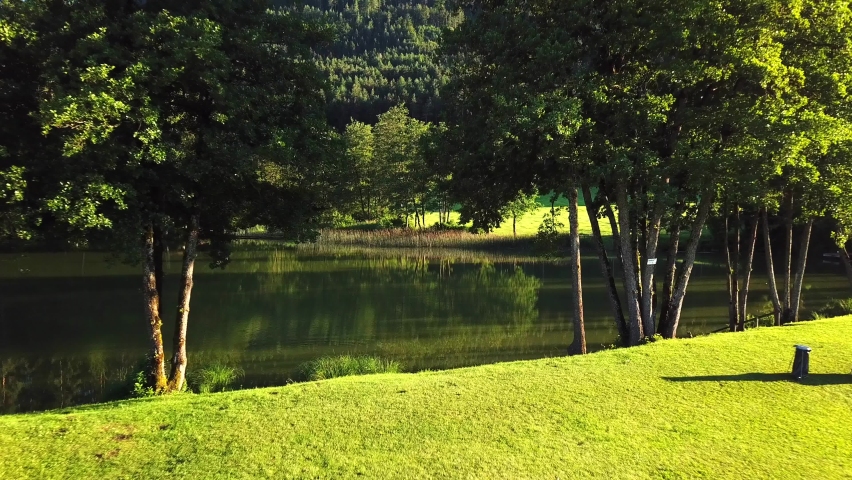 Aerial view of a hidden pond surrounded by trees on an Austrian mountain valley, on a sunny day