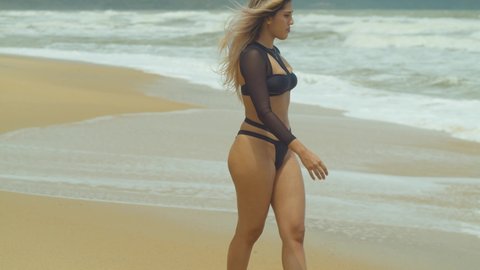Blonde hair sexy latina girl walks into the ocean with the waves crashing at her feet