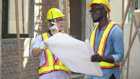 asian foreman and african american architect discuss with blueprint outdoors on construction site at village . contractor worker Inspection with builder . Engineer and foreman . quality control 