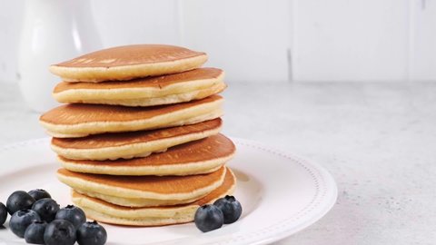 Pancake stack with blueberries and maple syrup on a white plate, copy space.