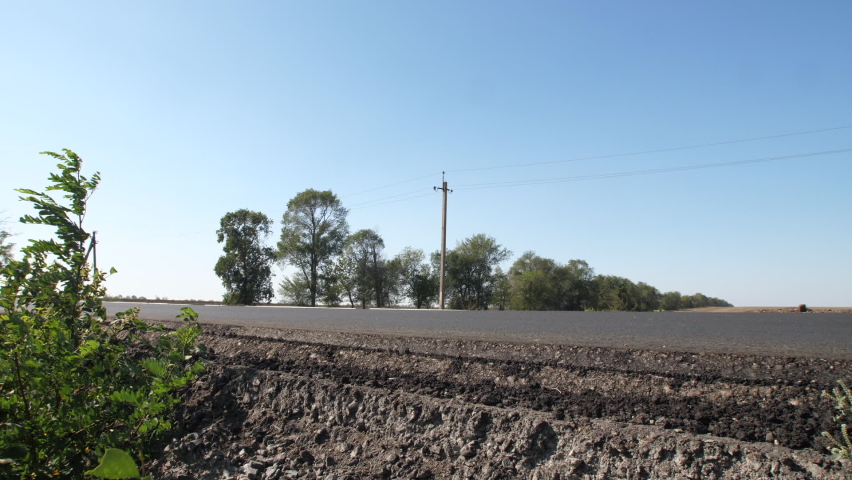 Truck passing roadside camera in the countryside, blues sky, trees backside, static shot. View from ground