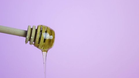 Honey drips from a wooden spoon, pink background. Natural food, healthy food, farming.