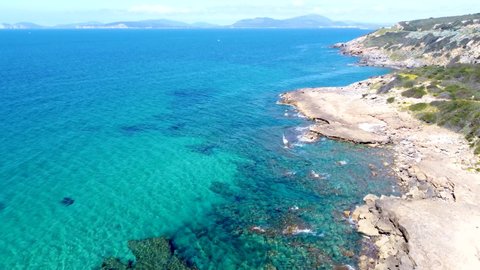 Overflying Alghero rocky shore and blue sea on a sunny day. Sardinia, Italy