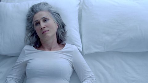 Thoughtful greyhaired woman covering with blanket, sleeping in bed, insomnia