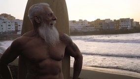 Fitness senior having fun surfing at sunset time - Sporty bearded man training with surfboard on the beach - Elderly healthy people lifestyle and extreme sport concept - Powered by Shutterstock - Get 15% off with code: PIKWIZARD15