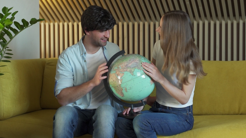 Married couple looks at the globe in the living room sitting on the sofa. Young couple choosing place for travel