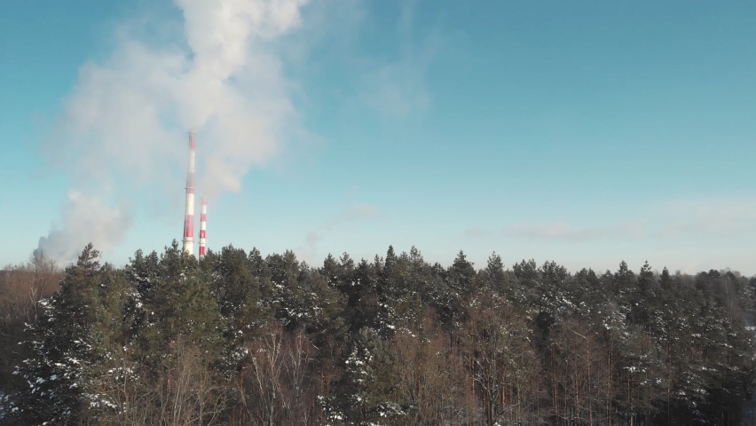 Aerial drone shot of white steam out of heat plant smokestacks during cold day in winter with city in the background. Clear blue sky sunny weather. Flying up ascending reveal from behind the trees | Shutterstock HD Video #1069857559