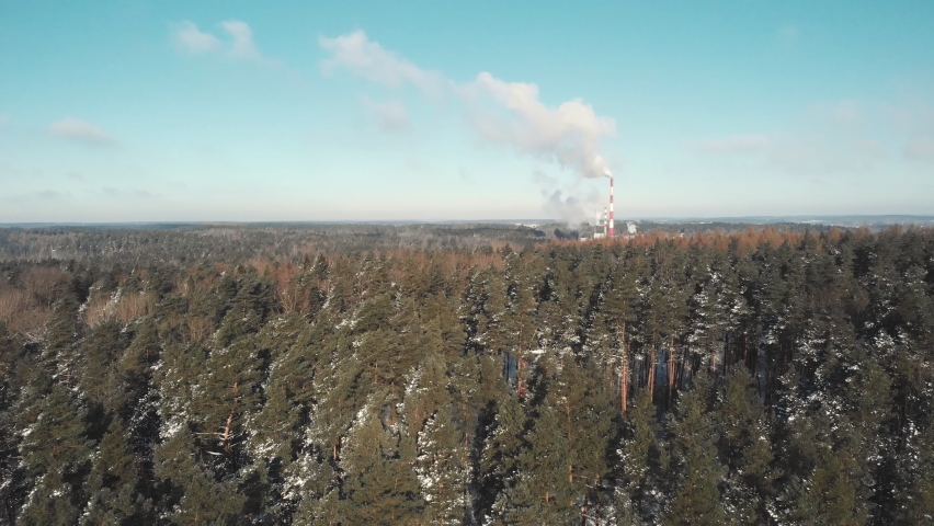 Aerial distant drone shot of heating power plant with white steam smoke coming out of the chimneys. Winter pine forest in the foreground with snow on the trees. Flying forward no camera motion | Shutterstock HD Video #1069858135