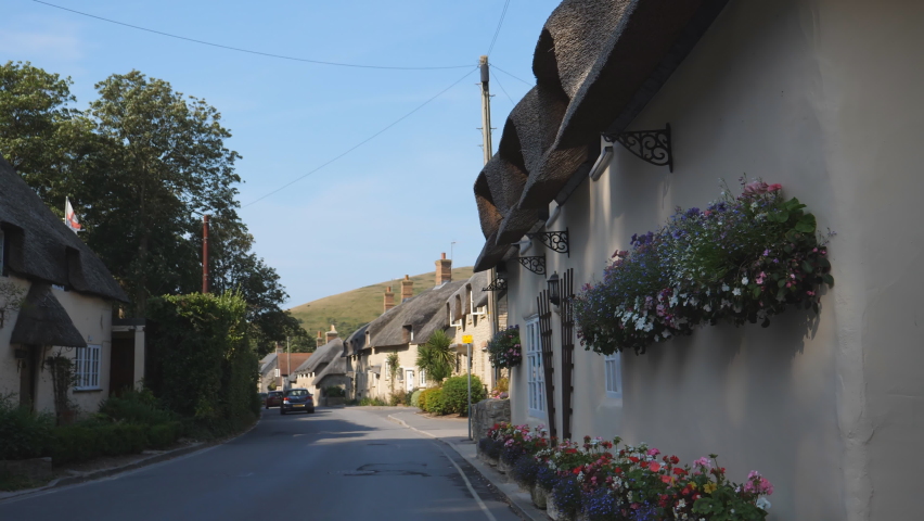 Flowers on the thatched house wall in a village of West Lulworth. Street view of traditional thatched cottages and tatty flag of England flying above roof.