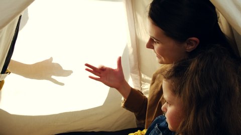 Loving father entertain little daughter and cute mother, sitting in tent spending weekend at home, mom with sweet small child enjoy watching puppet theater of shadows, young family play talking dogs