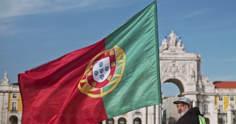 Lisbon, Portugal - Dec. 07, 2019: A bearded tourist man holding a Portugal flag at the Commerce Square.