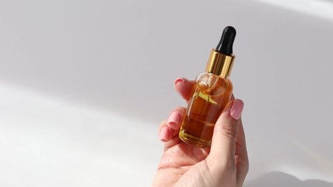 Beautiful female hand twirls in her hand and puts a small bottle with a pipette with golden colored oil