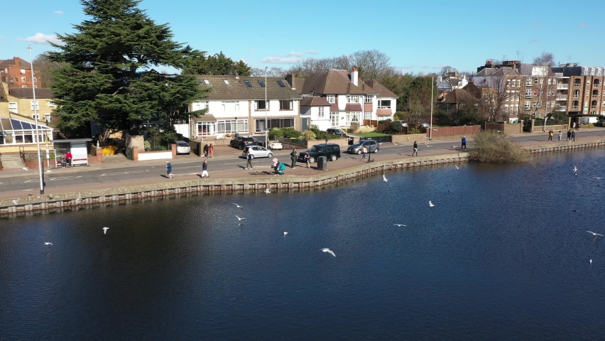 INTERESTING VIEW OF BIRDS FLYING OVER A POND IN THE CITY WITH PEOPLE WALKING ALONGSIDE
