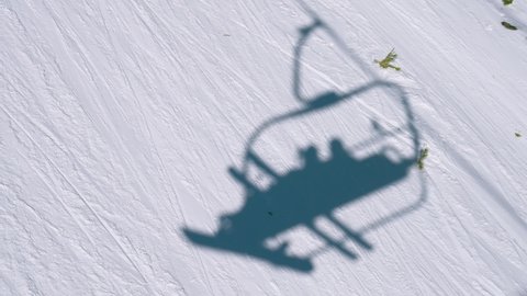 Shadow in the snow from the chair lift with a skier and snowboarder along a mountain ski run
