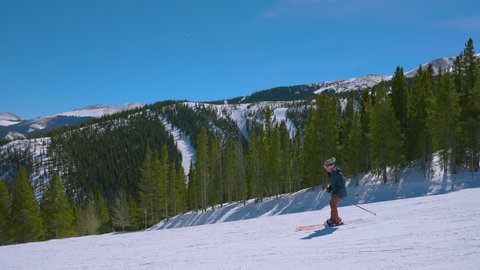 Slow-motion of one skier on a bright sunny day with other ski slopes in the distance along the rocky mountains