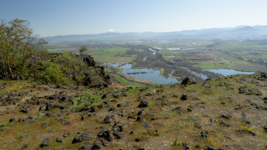 Walking and peering over a cliff into a valley with a river and volcano in the background on a sunny day. Taken on Lower Table Rock plateau in the Rogue Valley near Medford, Oregon with Mt Mcloughlin.