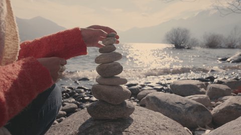 Woman stacking rocks by the lake, relaxing moment 