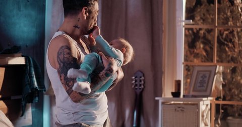 Tattooed fappy father puts the baby to sleep late at night, dad and son in the bedroom at night.	