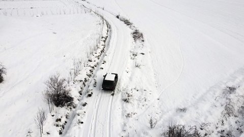 An aerial drone video following a Russian made 4x4 off-road Lada Niva vehicle driving along a snowy dirt road in Southern Albania in the winter.