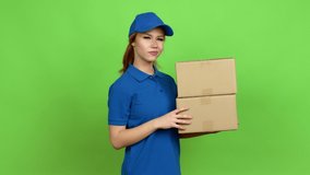 Young blonde teenager girl holding boxes for delivery listening something over isolated background. Green screen chroma key