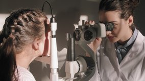 Medium closeup of female ophthalmology specialist doing eye checkup for little girl looking through phoropter machine sitting in sunlight filled doctor office - Powered by Shutterstock - Get 15% off with code: PIKWIZARD15