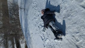on a sunny winter day, a little girl tumbles through the snow, rejoicing, vertical video shot on the phone