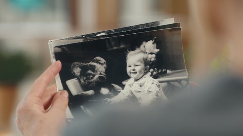 Senior woman looking at old photo album closeup. Mature female holding nostalgic memory of child at comfort modern flat. Casual elderly life and wrinkled skin of hands. Biography or history concept