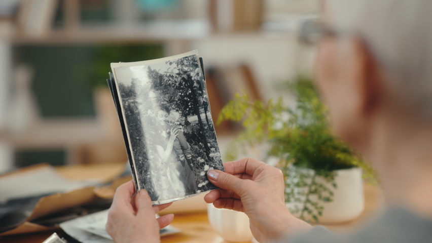 Senior 60s woman looking at old photo album closeup. Mature modern female holding nostalgic memory of baby and motherhood. Casual elderly life and wrinkled skin of hands. Biography or history concept Royalty-Free Stock Footage #1069898299