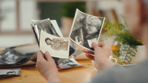 Senior 60s woman looking at old photo album closeup. Mature modern female holding nostalgic memory of baby and motherhood. Casual elderly life and wrinkled skin of hands. Biography or history concept